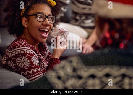 Primo piano di una ragazza che è eccitato perché un regalo ha ottenuto alla festa di Capodanno con i suoi amici in un'atmosfera festosa a casa. Natale, Capodanno, h Foto Stock