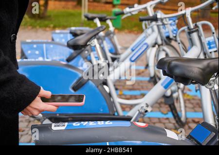 Primo piano di scansione femminile codice QR con telefono cellulare mentre si paga il noleggio biciclette sulla strada. Giovane donna che utilizza il servizio di noleggio biciclette urbano. Foto Stock