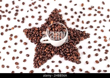 Tazza di caffè e stella fatta di caffè torrefatto in chicchi su sfondo bianco. Chicchi di caffè sparsi. Foto Stock