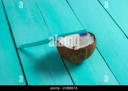 Il concetto di prodotti eco-compatibili per la cura dei denti. Spazzolino da denti e mezzo cocco su sfondo blu di legno Foto Stock