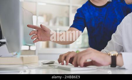 Un team di programmatori che lavorano insieme ai computer, gli analisti dei programmi puntano a un monitor per guidare i programmatori nella programmazione. Foto Stock