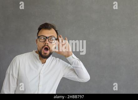 L'uomo con un'espressione scioccata tiene la sua mano all'orecchio per ascoltare la conversazione di qualcun altro. Foto Stock