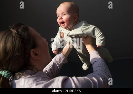 Donna che tocca la fronte con il suo neonato, sollevandolo contro la finestra a casa Foto Stock