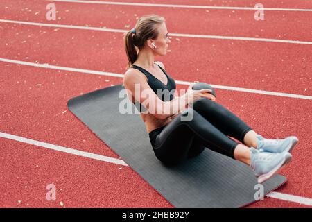 La giovane donna in forma perfezionerà il suo corpo mentre fa l'esercitazione con la sfera di medicina sul tappeto alla pista dello stadio con rivestimento rosso. Stile di vita sano Foto Stock