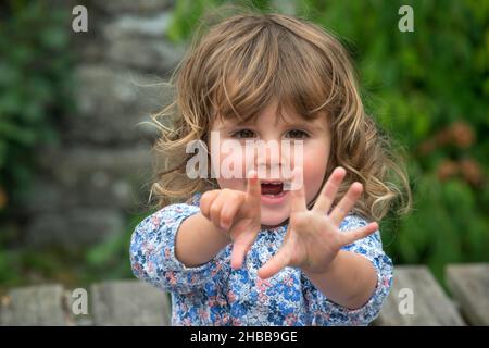 Ragazza di due anni, bionda, all'aperto, contando sulle sue dita Foto Stock