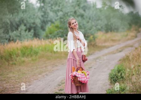 Giovane donna bionda con capelli lunghi in stile retrò vintage abiti con cestino pic-nic a piedi sul pianerottolo Foto Stock