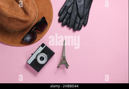 Jorney a Parigi. Accessori da donna (cappello, guanti, occhiali da sole), macchina fotografica retrò, figurina della torre Eiffel su sfondo rosa. Vista dall'alto Foto Stock