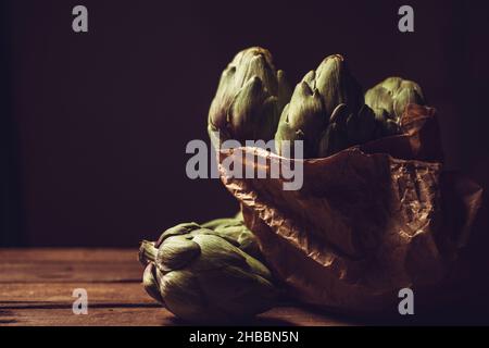 diversi carciofi all'interno di un sacchetto di carta su un tavolo di legno con spazio di copia, ancora vita, con texture e colore Foto Stock