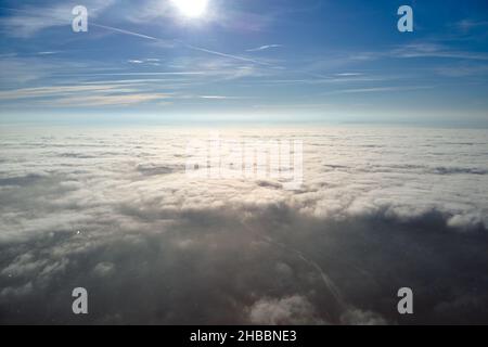 Vista aerea dalla finestra dell'aeroplano ad alta quota della città lontana coperta con strato di smog sottile e nubi distanti in serata. Foto Stock