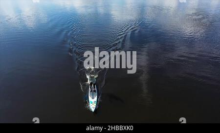Vista dall'alto di un uomo che pratica su una tavola da surf con una pagaia a remi nel lago, sport e stile di vita concetto. Antenna di un uomo in piedi su una tavola da surf e. Foto Stock