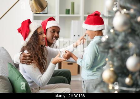 Piccolo ragazzo afro-americano che porta i suoi genitori gustoso cioccolata calda la vigilia di Natale Foto Stock