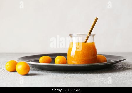 Vasetto di gustosa marmellata di kumquat e frutta fresca su sfondo chiaro Foto Stock