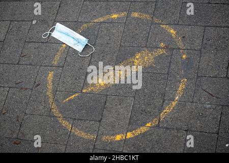 17 dicembre 2021, bassa Sassonia, Osnabrück: Una maschera usata si trova su un marciapiede accanto al pittogramma per una 'vaccinazione' contro il virus Covid 19. Foto: Friso Gentsch/dpa Foto Stock