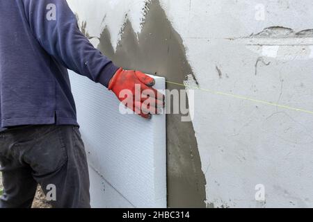 Addetto alla costruzione che installa fogli di isolamento in polistirolo sulla parete della facciata della casa per la protezione termica. Foto Stock