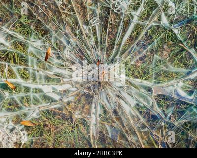 Un vecchio vetro rotto con molte crepe giace su erba verde. Foto a schermo intero Foto Stock