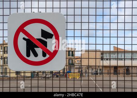 Primo piano di un cartello di divieto di accesso ai cani. Sullo sfondo, fuori fuoco, una recinzione metallica che delimita un parco giochi per bambini Foto Stock