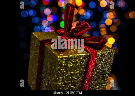 Scatola regalo d'oro con un nastro rosso su sfondo bokeh di Natale luci Foto Stock