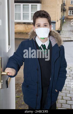 Un ragazzo della scuola che ritorna dalla scuola con una maschera facciale sopra per proteggere contro i virus Foto Stock