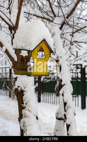 una piccola casa ornitologica coperta di neve è appesa ad un albero in inverno. Foto di alta qualità Foto Stock