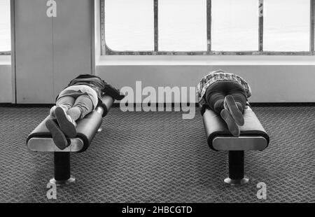 Due turisti riposano su panchine morbide nella zona pubblica, viaggiando a bordo di un grande traghetto per l'oceano senza pagare un soggiorno in cabina. Foto Stock