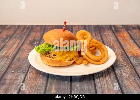 Hamburger di manzo con pane brioche, salsa di panna, lattuga e anelli di cipolla fritta croccanti su un piatto bianco Foto Stock