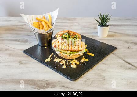 Delizioso sandwich al salmone tempura con hamburger di panino, avocado, alghe di wakame, uova di masago e patatine fritte Foto Stock