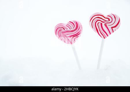 Due lecca rosa a forma di cuore. Caramelle al caramello su un bastone su sfondo bianco. Dolce regalo per San Valentino. Spazio di copia Foto Stock