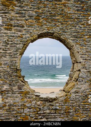 Colpo verticale di un grande buco nella vecchia parete di mattoni che si affaccia sulle onde del mare in una giornata cupa Foto Stock