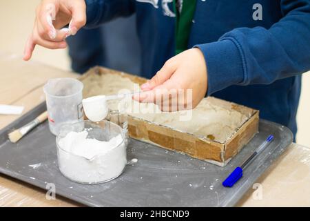 Le mani del bambino stanno preparando una miscela di gesso nel laboratorio per la ricerca Foto Stock