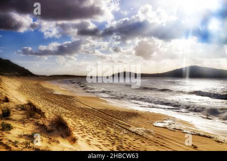 Tempesta dell'oceano Pacifico sulla spiaggia di Fingal a Port Stephens dell'Australia con il sole che sale attraverso le nuvole di tempesta. Foto Stock