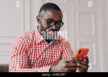 Allegro uomo biraciale millenario con smartphone, seduto alla scrivania Foto Stock