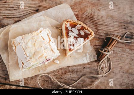 pezzo di rotolo di meringa e cheesecake al caramello su carta pergamena, su sfondo di legno, vista dall'alto Foto Stock