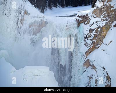 Cascate superiori ghiacciate e innevate del fiume Yellowstone nel parco nazionale di Yellowstone nel Wyoming con scogliere rocciose su entrambi i lati. Foto Stock