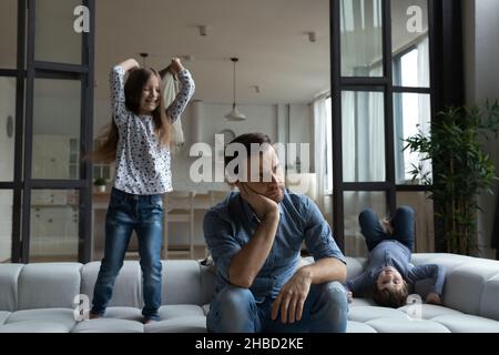 Padre stanco seduto sul divano con figlia e figlio rumorosi Foto Stock