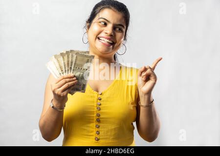 Una bella donna indiana in abito giallo con contanti sorridente alla macchina fotografica su sfondo bianco Foto Stock