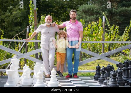 Ritratto di nonno padre e figlio che gioca a scacchi. Uomini felici in diverse età giocando a scacchi gioco da tavolo. Generazione di tre uomini. Foto Stock