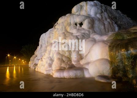 Formazioni geologiche bianche lungo la strada principale per Pamukkale con luci di strada sullo sfondo di notte. Treventines, acque minerali curative in Turchia Foto Stock