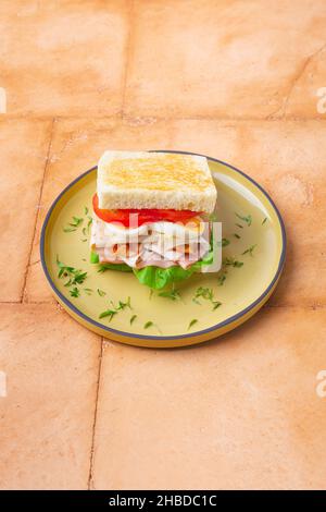 Sandwich Big Club con prosciutto, pancetta, pomodoro, cetriolo, formaggio, uova ed erbe Foto Stock