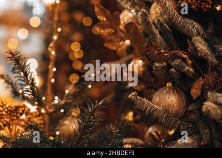 Sfera di Natale d'oro e ghirlanda luminosa appesa sull'albero di Natale. Composizione fata vacanza inverno e dettagli magici. Foto Stock