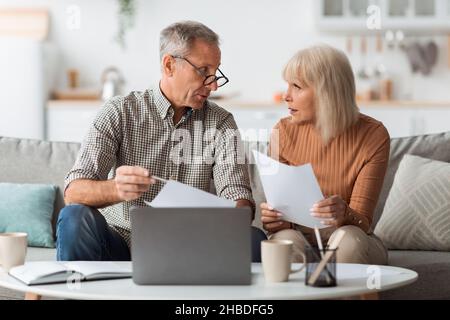 Senior Couple Holding Papers lettura documenti seduti al laptop Indoor Foto Stock