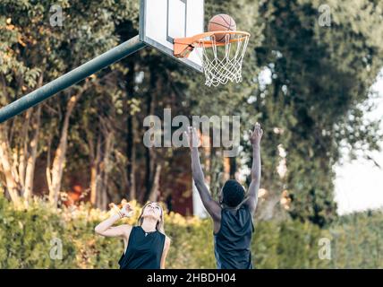 Palla che va in un cestino di basket, mentre alcuni amici multietnici stanno giocando Foto Stock