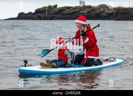 North Berwick, East Lothian, Scozia, Regno Unito, 19th dicembre 2021. Una donna che indossa un costume di Babbo Natale porta un ragazzino fuori nel Firth of Forth su un paddle board Foto Stock