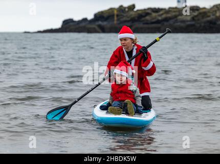 North Berwick, East Lothian, Scozia, Regno Unito, 19th dicembre 2021. Una donna che indossa un costume di Babbo Natale porta un ragazzino fuori nel Firth of Forth su un paddle board Foto Stock