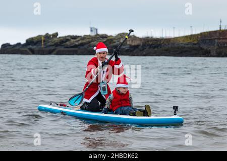 North Berwick, East Lothian, Scozia, Regno Unito, 19th dicembre 2021. Una donna che indossa un costume di Babbo Natale porta un ragazzino fuori nel Firth of Forth su un paddle board Foto Stock