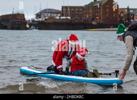 North Berwick, East Lothian, Scozia, Regno Unito, 19th dicembre 2021. Una donna che indossa un costume di Babbo Natale porta un ragazzino fuori nel Firth of Forth su un paddle board Foto Stock