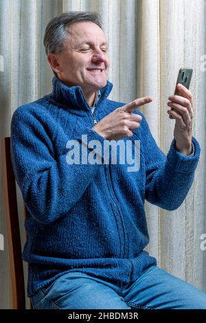 L'uomo seduto utilizza uno smartphone che punta verso lo schermo durante una videochiamata Foto Stock