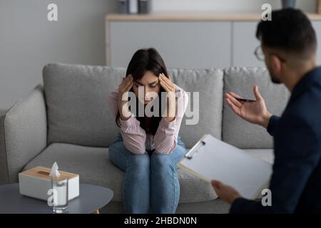 Concetto di psicoterapia. Donna araba depressa che tocca la testa, cercando aiuto professionale con disturbo mentale Foto Stock