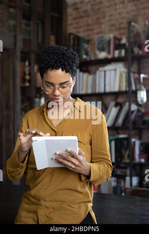 Immagine verticale concentrata giovane afroamericana usando il tablet. Foto Stock
