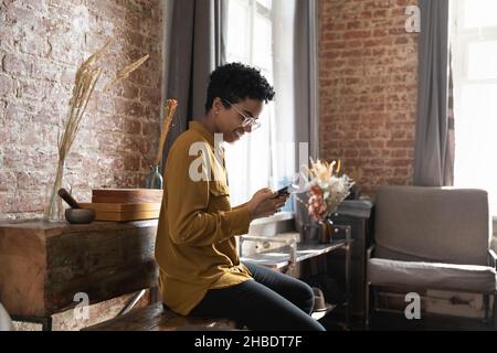 Gioiosa giovane afroamericana che usa il cellulare a casa. Foto Stock