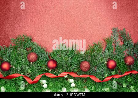 Rami di abete con palle rosse lucide e opache, nastro con bokeh su sfondo brillante. Natale, Capodanno. Spazio di copia Foto Stock